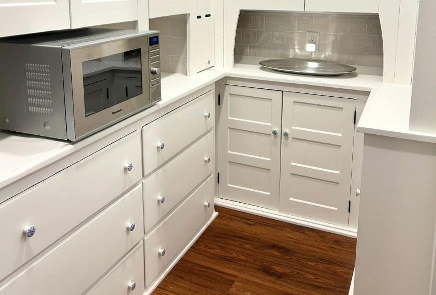 A small kitchen area with white cabinets and drawers, a microwave on the countertop, a silver tray, and a wood floor—perfect inspiration for your Oberlin kitchen remodel.