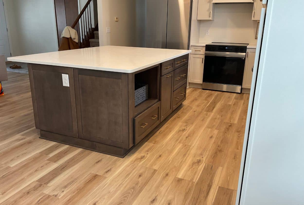 A stunning Amherst Kitchen Remodel featuring light wood flooring, a large island with brown cabinets and white countertop, an electric stove, and stainless steel appliances. See this kitchen before after transformation!.