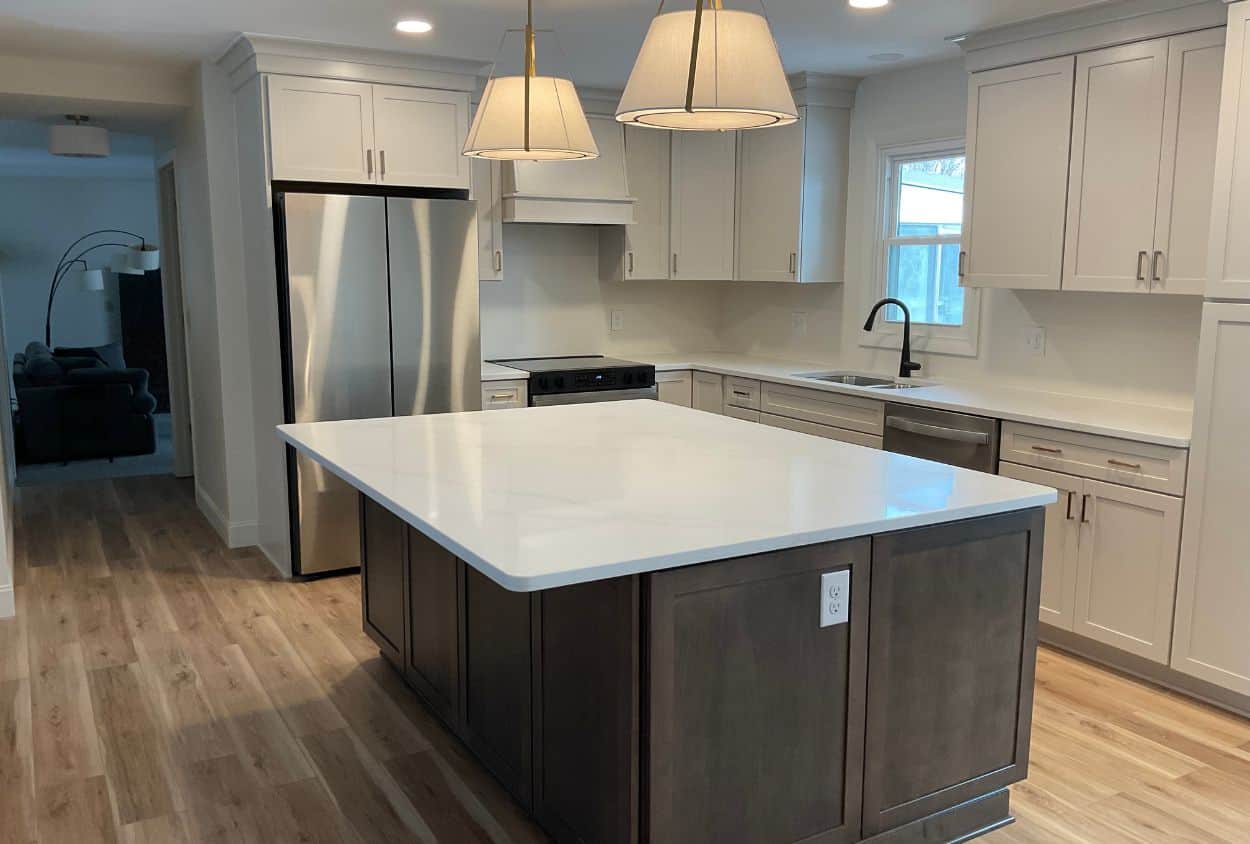 Modern Amherst kitchen remodel featuring light wood flooring, white cabinets, stainless steel appliances, a large island with a dark base, and two pendant lights illuminating the space.