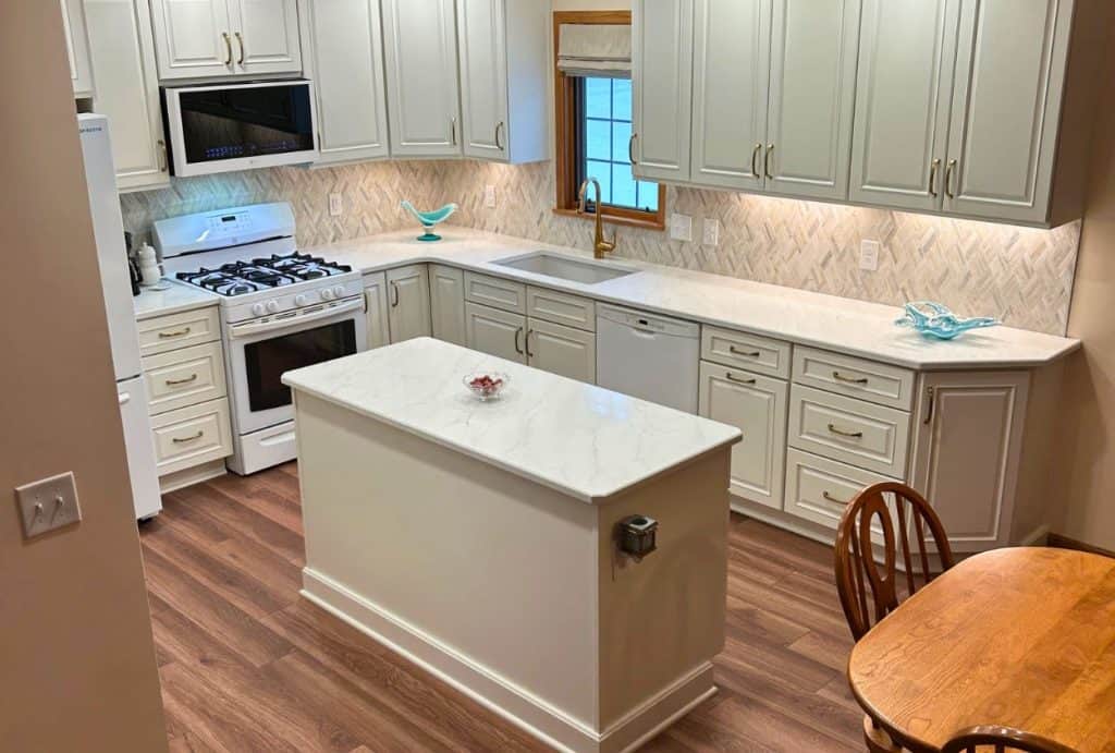 Modern kitchen remodel Amherst with white cabinets, marble countertops, a small island, gas stove, and a wooden dining table with chairs on a wood floor—see the stunning Amherst kitchen remodel before after transformation.